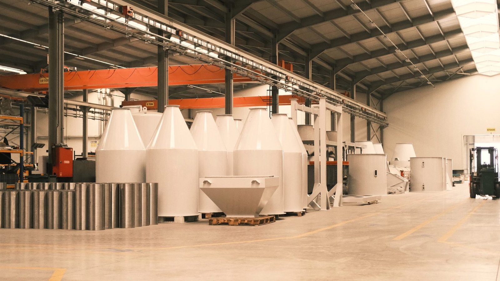 Wide view of a coating shop with freshly coated white vessels standing under an overhead conveyor line.