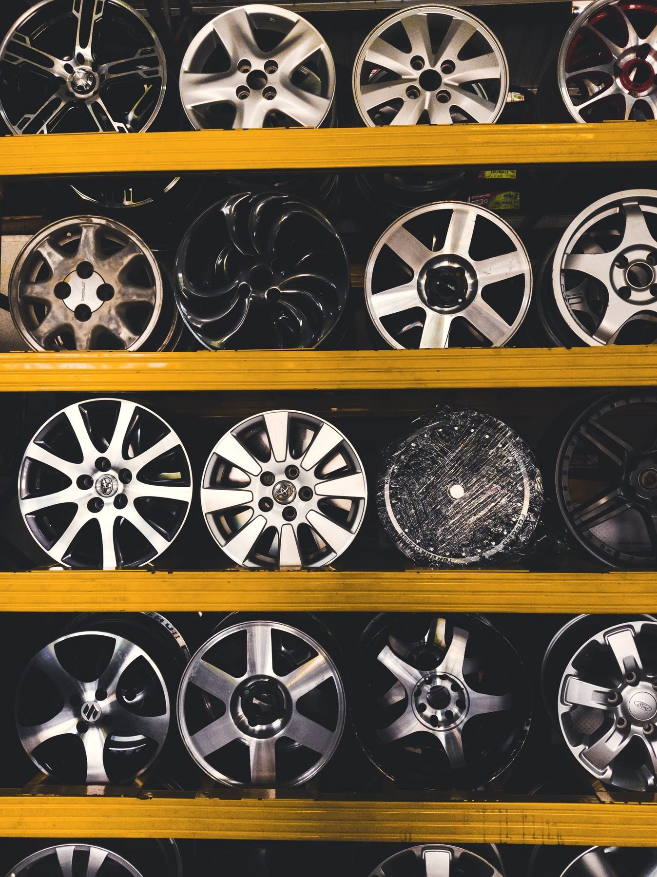 Bare alloy rims stacked in rows on yellow steel shelving.