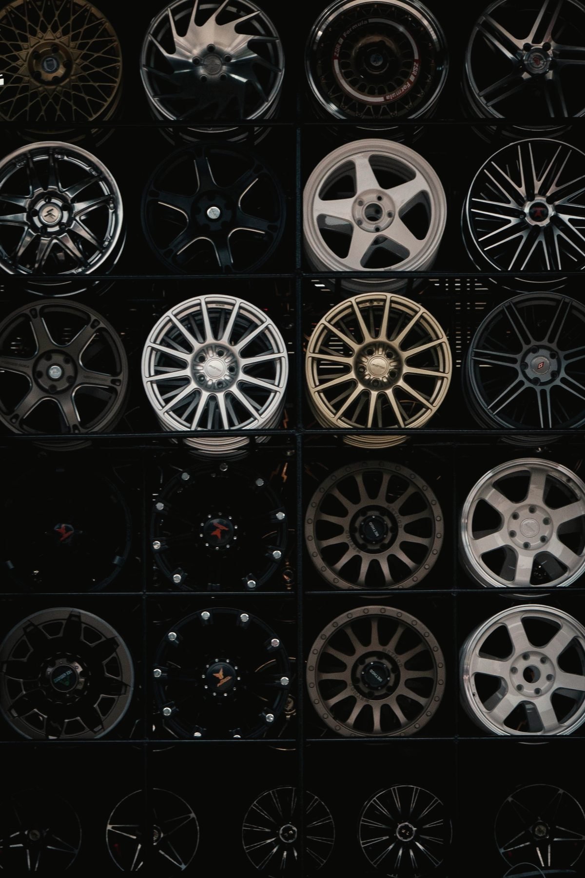 A wall of alloy wheel faces in silver, black and gold against a dark background.